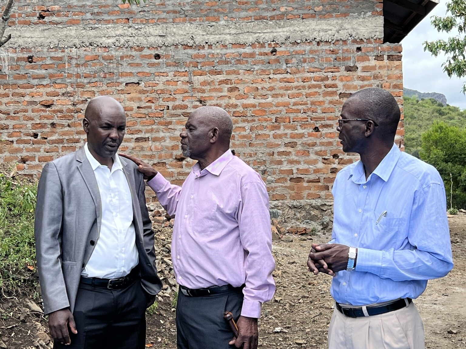 Three local leaders speaking together beside a brick building