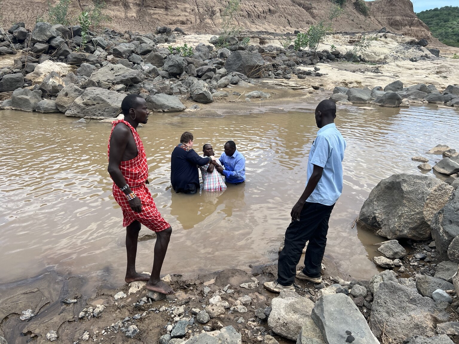People gathered together in a river surrounded by rocks and hills